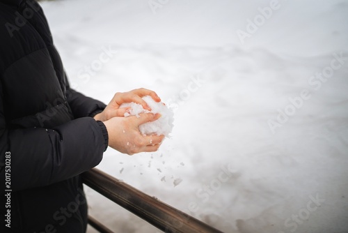 Teenager forming a large snowball from freshly fallen snow, enjoying winter outdoor play.