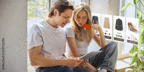 Foto Couple shopping for clothes online with tablet and floating fashion product cards at home