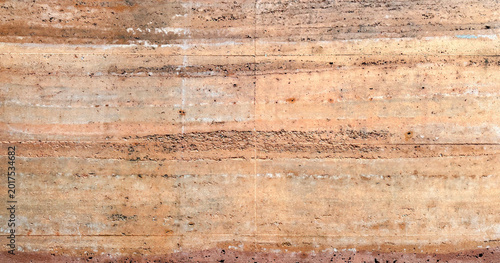 Rammed earth wall texture with horizontal layers of sedimentary rock and natural soil colors of orange brown and tan for architecture and sustainable building design background pattern material.