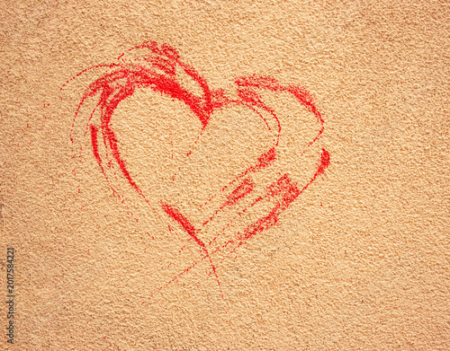 simple red heart shape drawn with chalk or crayon on a rough beige textured wall, symbolizing love and street art