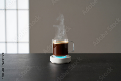 Hot coffee in clear mug on smart coaster with glowing blue light