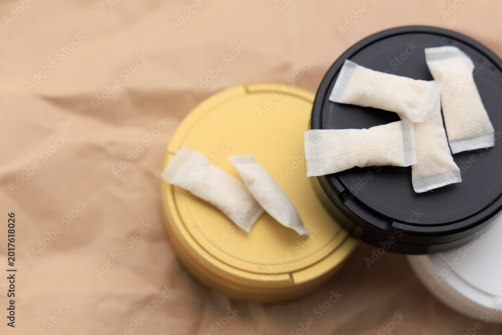 Naklejka premium Different colored containers hold snus pouches with nicotine pads placed on a brown background