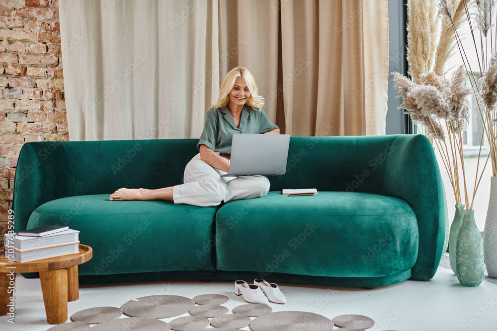 Obraz premium Blonde woman finds joy in remote work from a stylish, modern living room setup