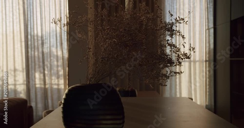 Dried flowers in a modern vase on a dining table. Sunlight streams through sheer curtains, creating a warm, inviting atmosphere. Perfect for home decor, lifestyle, and interior design projects.