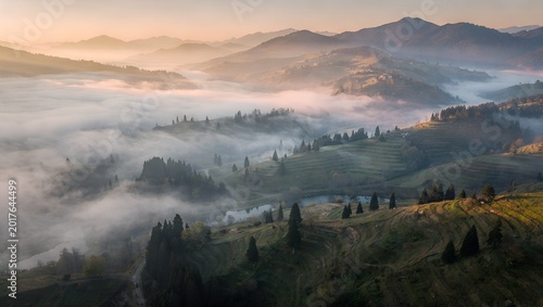 Aerial view of rolling hills, foggy valleys, and mountains at sunrise