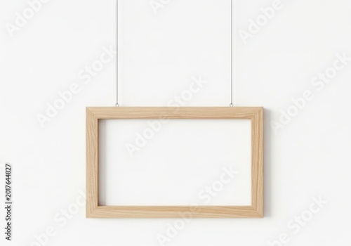 Empty rectangular wooden picture frame hanging by wires on a plain wall surface
