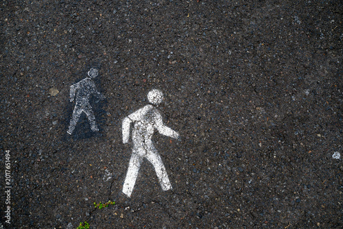 Stenciled white pedestrian symbols painted on dark weathered asphalt pavement