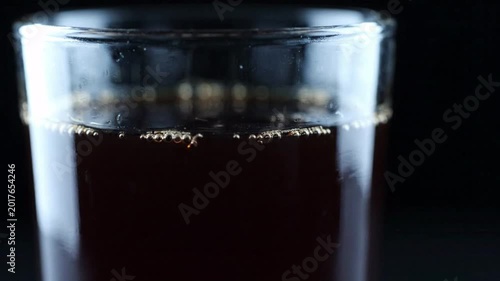 Close up of dark beverage with effervescent bubbles rising in clear glass, refreshing drink, black background