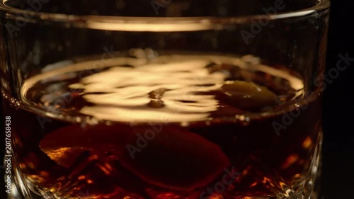 Amber colored spirit being poured into a crystal glass with an orange peel garnish, dark background, luxurious ambiance