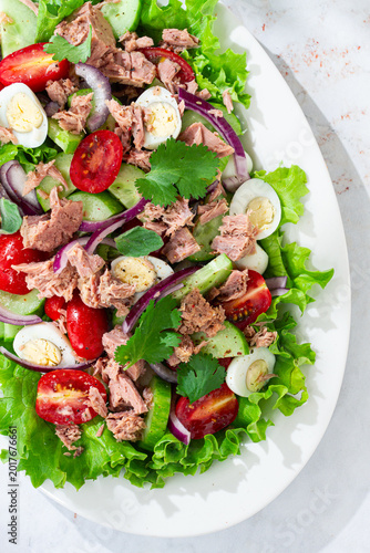 salad with canned tuna, cherry tomatoes, cucumber, and quail eggs on a white plate