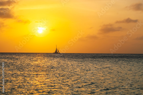 Canvas-taulu the sun setting over the ocean, with the silhouette of a sailboat on the horizon