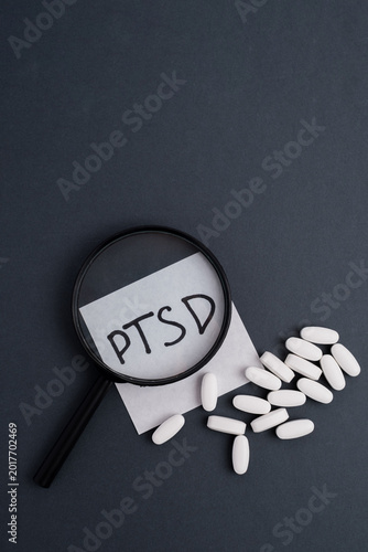 A magnifying glass over a PTSD label with scattered white pills on a dark grey background