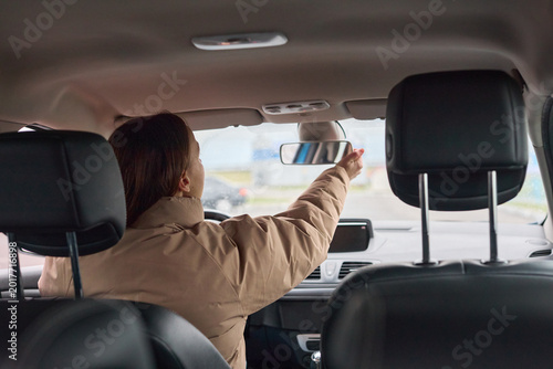 Fotografi Woman adjusting her rearview mirror inside a car, ensuring clear visibility for