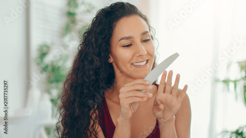 Bild auf Leinwand A woman smiles while filing her nails with a nail file in a well-lit room