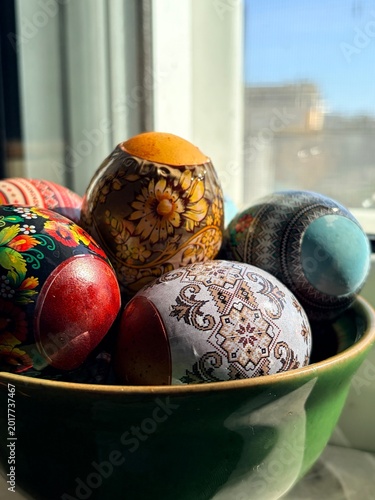 Colorful decorative traditional easter eggs with floral and geometric patterns in green bowl on window 