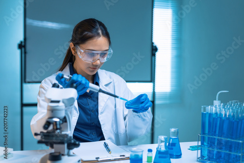 Young Asian scientist conducting research, dropping liquid into a petri dish, surrounded by lab equipment and blue solutions