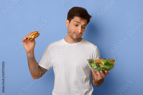 Fotografie A person stands with a burger in one hand and a salad bowl in the other
