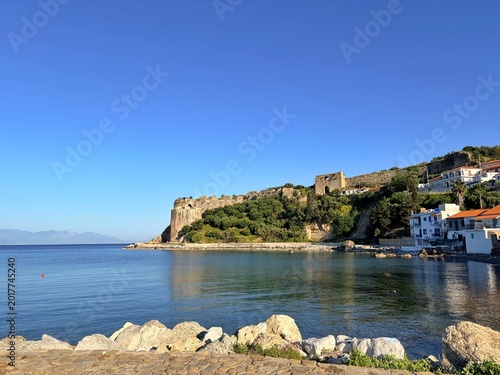 Koroni Castle, Mediterranean seaside village with ancient stone castle ruins on hill under clear blue sky