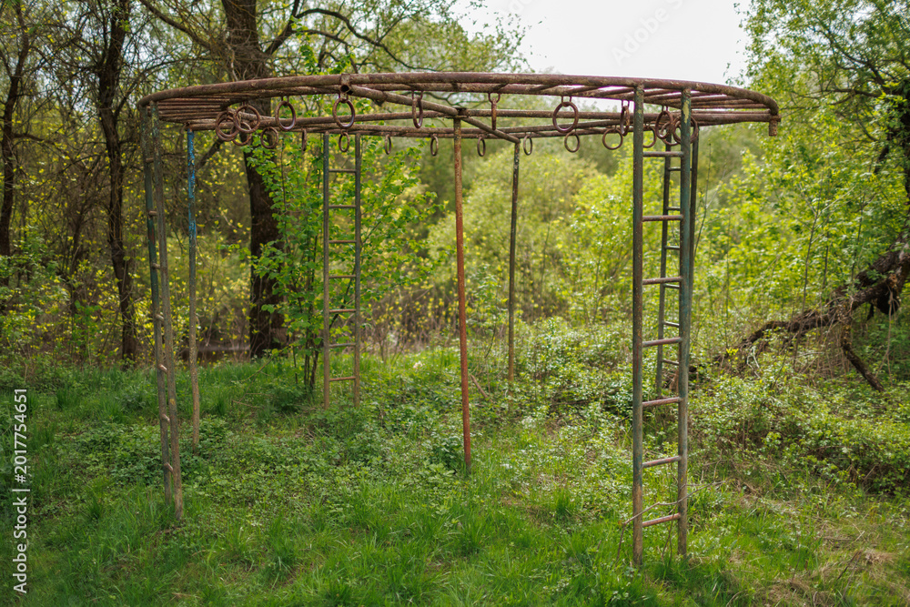 Fototapeta premium Large circular metal jungle gym in a wooded area with rusty ladders and hanging rings