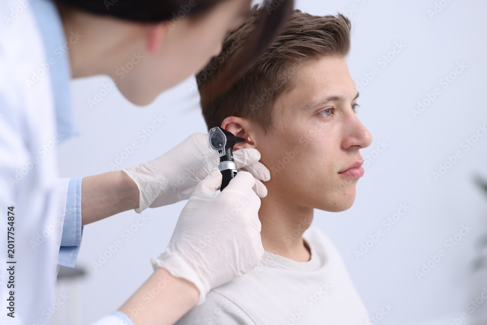 Fototapeta premium Hearing test. Doctor examining man's ear with otoscope in clinic, closeup