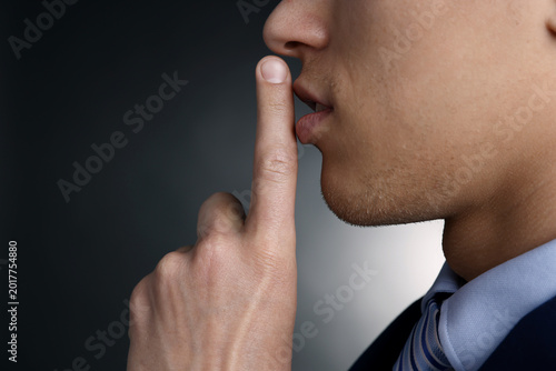 Foto Businessman in suit showing hush gesture on grey gradient background, closeup