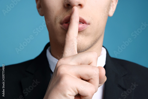 Photos Businessman in suit showing hush gesture on light blue background, closeup
