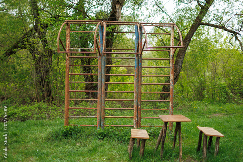 Rusted wall bars and a simple wooden table with benches in a green spring forest park area