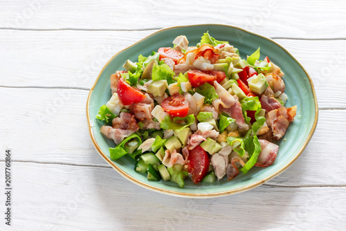 Cobb salad with chicken, avocado, tomatoes, eggs and bacon served on a light blue ceramic plate on a white rustic wooden table.