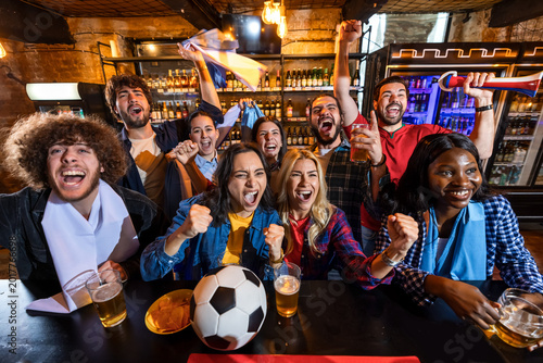 Energetic group of friends cheering during live soccer match in pub