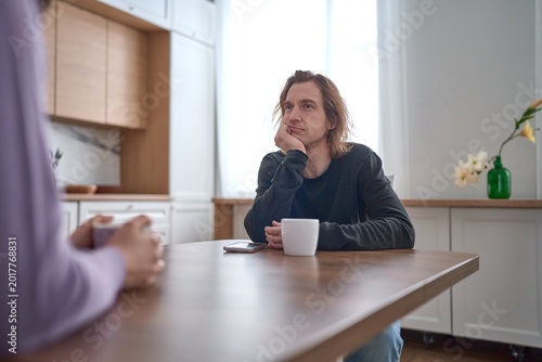Bored man resting head on hand during dull kitchen conversation