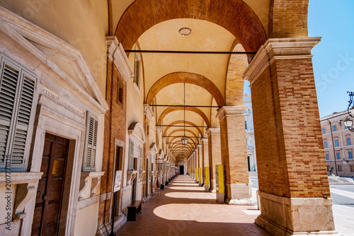 Long portico colonnade with repeating arches and columns creating a deep perspective and strong light and shadows, part of the Sanctuary of the Holy House in Loreto, Marches, Italy