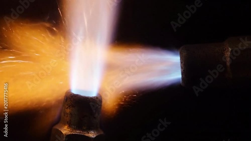 close up of a welding torch emitting blue and orange flames in darkness, sparks flying, ideal for industrial concepts