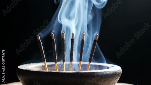 Incense sticks burning and releasing aromatic smoke in a dark, moody setting, creating a serene atmosphere for meditation or relaxation