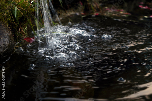 Fotografie Small water fountain pouring into a dark pond with bubbles