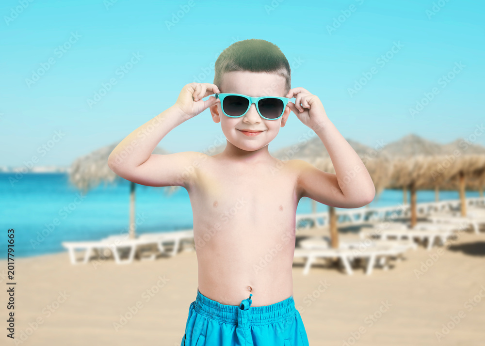 Fototapeta premium Adorable little boy in swimwear with sunglasses on beach