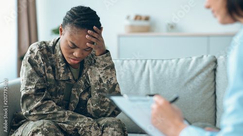 Valokuva A military service member sits on a couch with their head in their hands, showing signs of distress