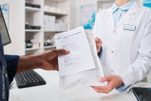 Tableau sur toile Close up of pharmacist handing prescription pickup package to middle aged man at