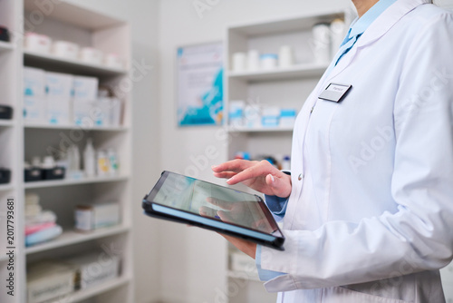 Close up of middle aged woman healthcare worker using tablet in pharmacy, managing inventory and patient records. Ideal for medical technology, digital healthcare, clinic workflow
