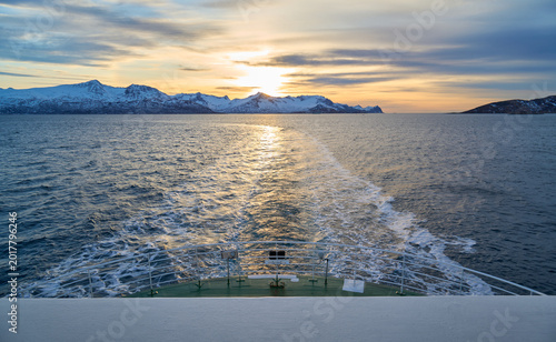 Wake of a ferry in Norwegian fjord during golden hour sunset with glowing orange sky and water
