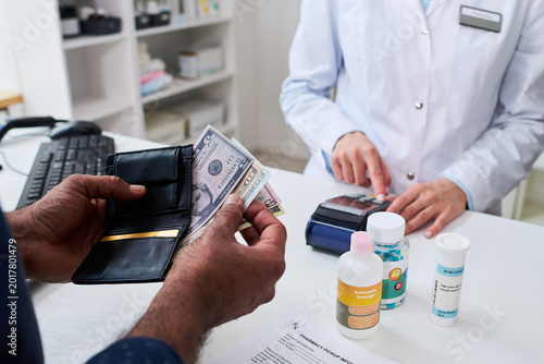 Close up of man paying for prescription medicine at pharmacy counter while pharmacist processing card terminal, illustrating healthcare purchase and retail pharmacy marketing