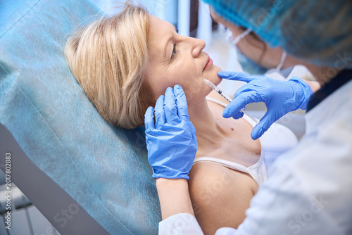 Photos Middle-aged woman receiving cosmetic injection in medical room