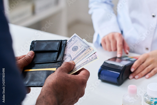 Close up of middle aged man holding wallet and cash while pharmacist processing card terminal payment at counter, showing healthcare purchase and pharmacy checkout use in retail health marketing