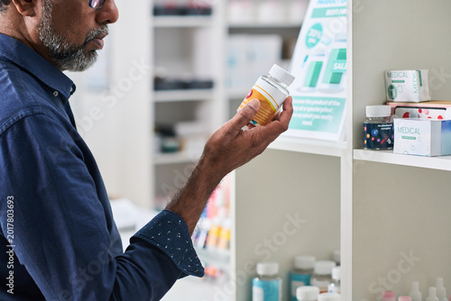 Tableau sur toile Middle aged man examining supplement bottle in pharmacy aisle, comparing product information for purchase decision