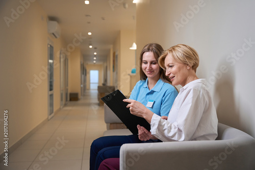 Two women discussing clipboard in hospital hallway, daytime