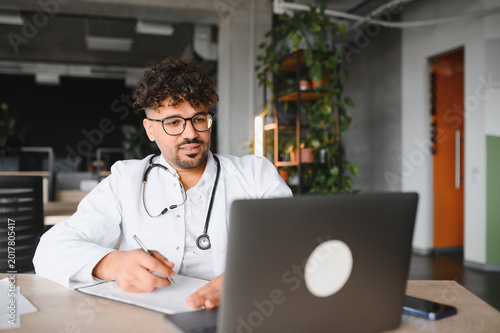 Arab doctor attending online meeting and taking notes on clipboard