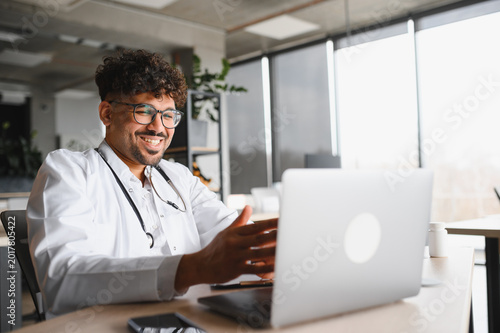 Arab male doctor having video call on laptop in modern office