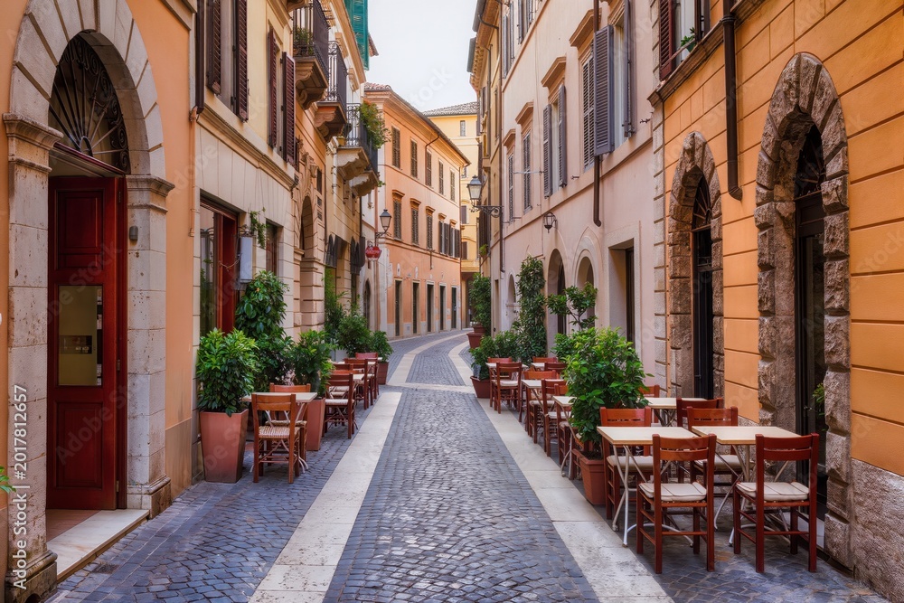 Fototapeta premium Rue pavée pittoresque avec terrasses de cafés et balcons fleuris dans une vieille ville italienne
