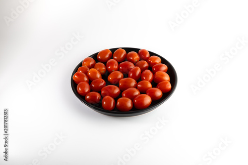 Fresh cherry tomatoes on black plate isolated on white background minimal food photography