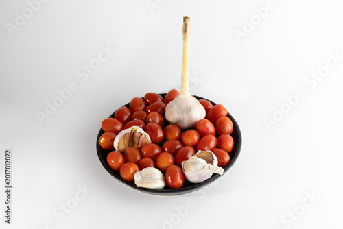 Cherry tomatoes and garlic on black plate isolated on white background healthy food concept