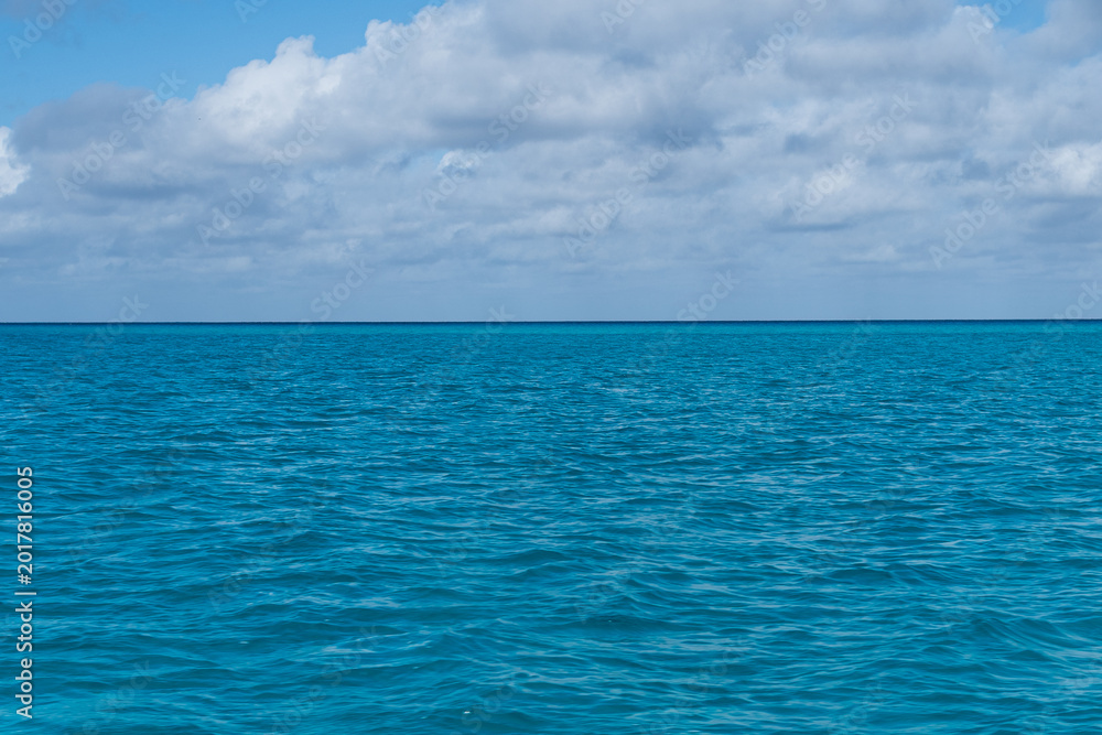 Fototapeta premium Calm blue ocean under blue sky with puffy clouds